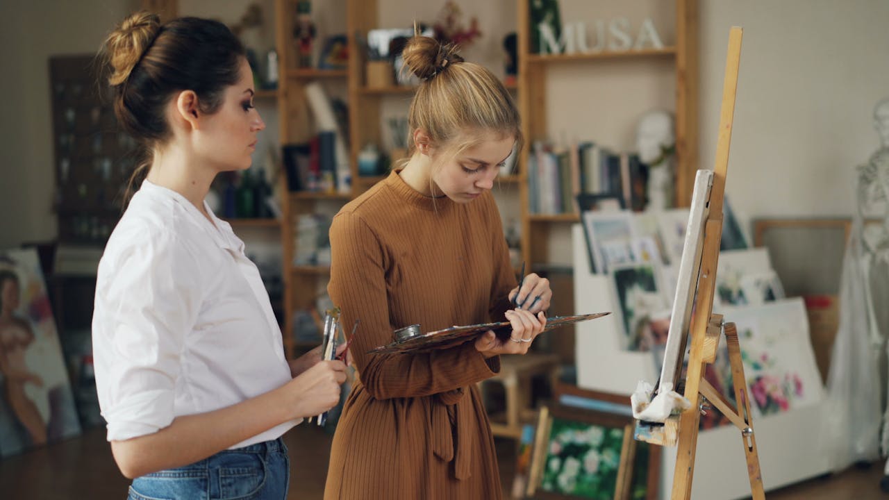 Two young women engaged in painting activities in an art studio, embracing creativity.